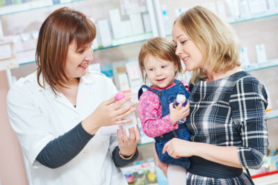 pharmacist chemist woman demonstrating cream gel to child girl with mother in pharmacy drugstore
